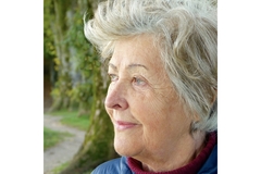 An elderly woman stares out of a window and smiles.